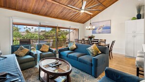 Un salón espacioso con techo de madera, un conjunto de sofá azul, una mesa de centro de vidrio y vistas al exterior.
