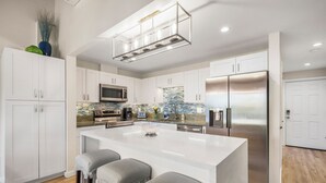 Una cocina moderna con armarios blancos, un refrigerador de acero inoxidable, una isla grande con taburetes de bar y un salpicadero de azulejos.