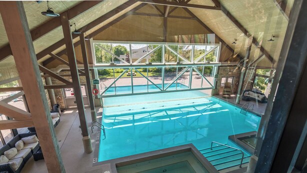 Piscina interna con vista aperta sull'esterno, area idromassaggio separata e zona relax coperta con cuscini.