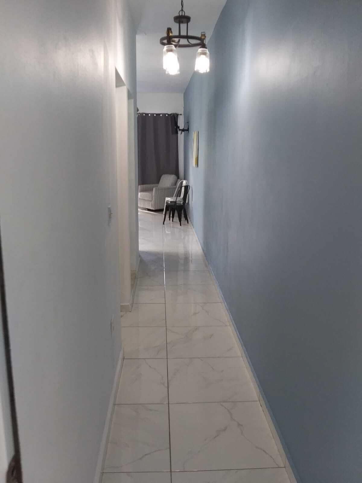 A hallway with light blue walls, a tiled floor, and a ceiling light fixture.