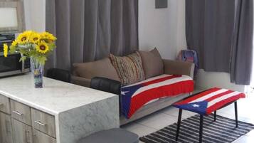 A modern living room with a sofa, a coffee table with a flag design, a vase with sunflowers, and a trash bin.