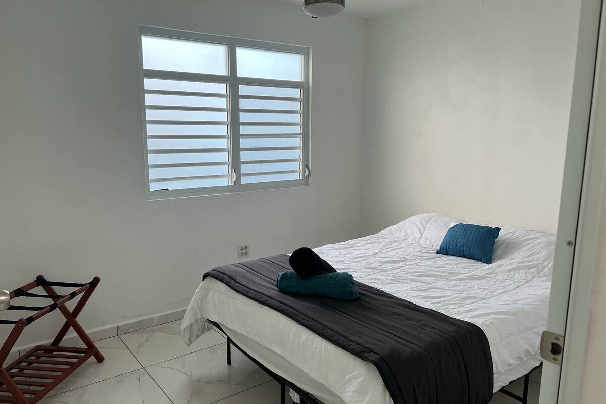 A bedroom with a bed, a window, a ceiling fan, and a wooden chair.