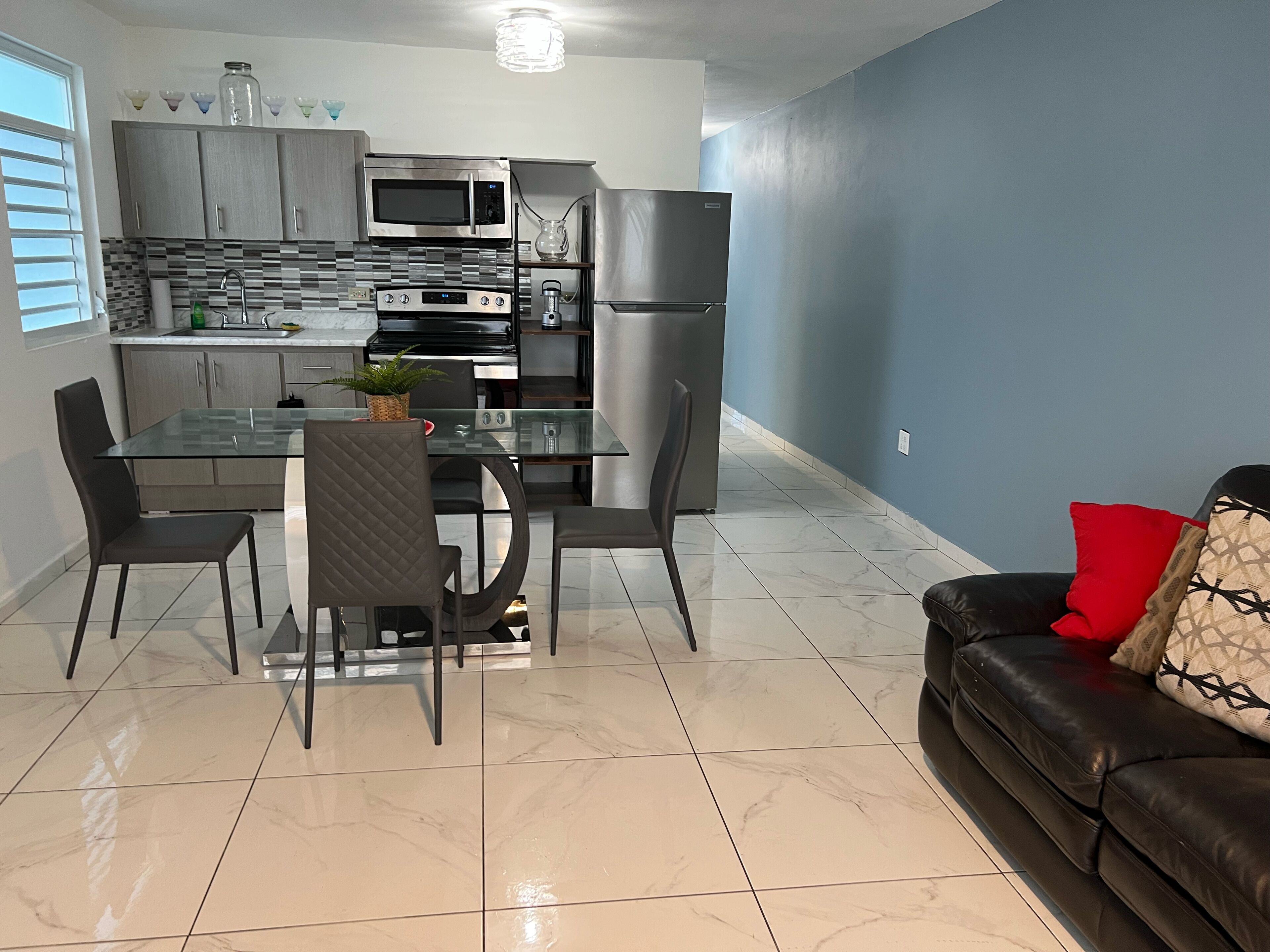 Una cocina moderna con comedor, que incluye una mesa y sillas de vidrio, un sofá de cuero negro y una pared azul de acento.