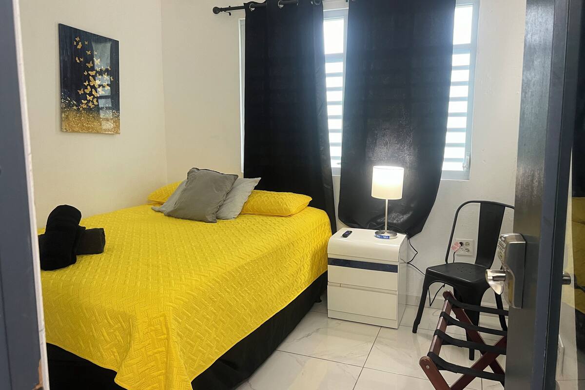A hotel room with a bed, a nightstand, a desk, a chair, and a window with curtains.