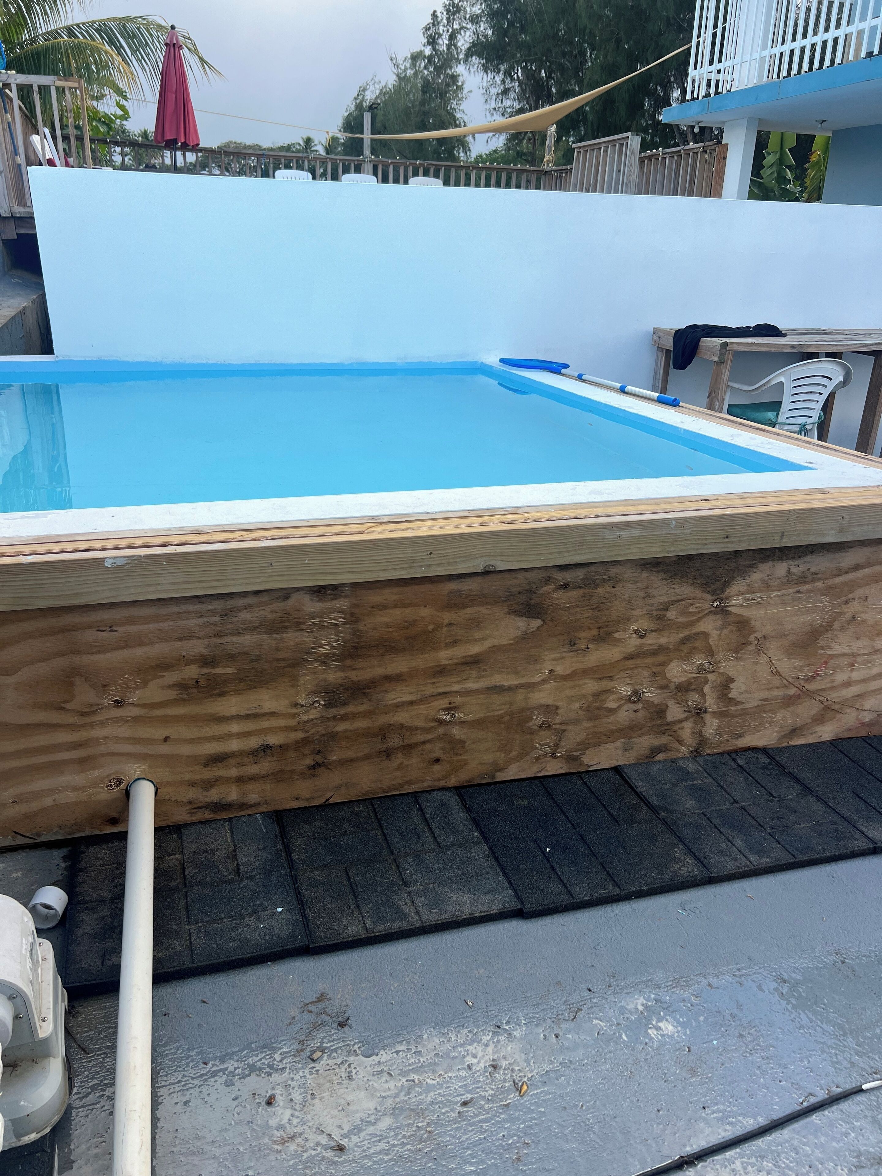 Una piscina de madera con revestimiento azul, rodeada por una cubierta de madera y una valla blanca.