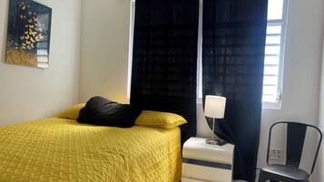 A bedroom with a bed, a nightstand, a chair, a window with curtains, and a wall art piece.