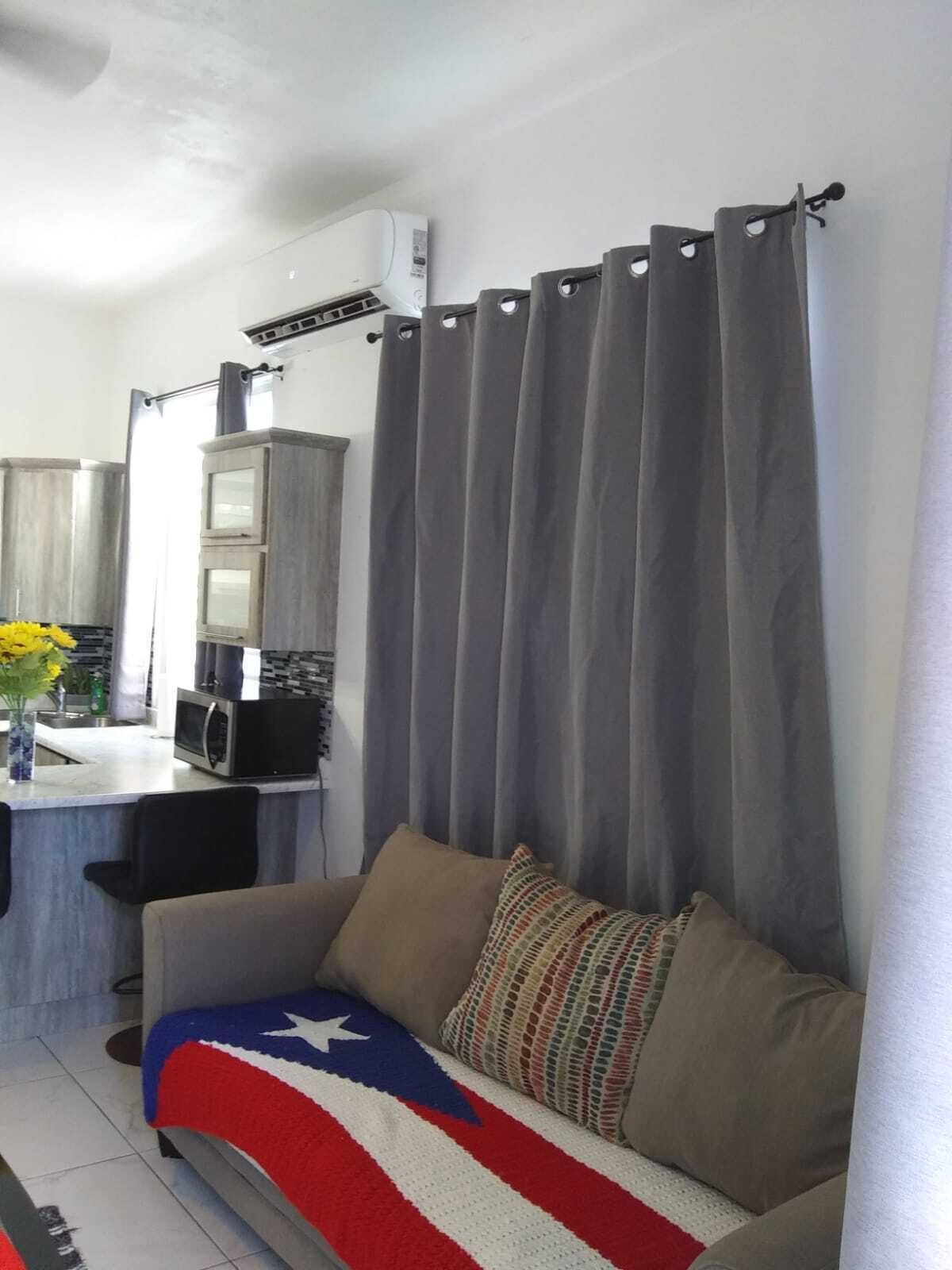 A living room with a sofa, a small kitchen area with a microwave, and a grey curtain.