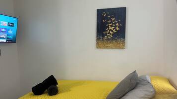 Ein Zimmer mit einem gelben Bett, einem grauen Kopfkissen mit schwarzem Muster und einem Schmetterlingsbild an der Wand.