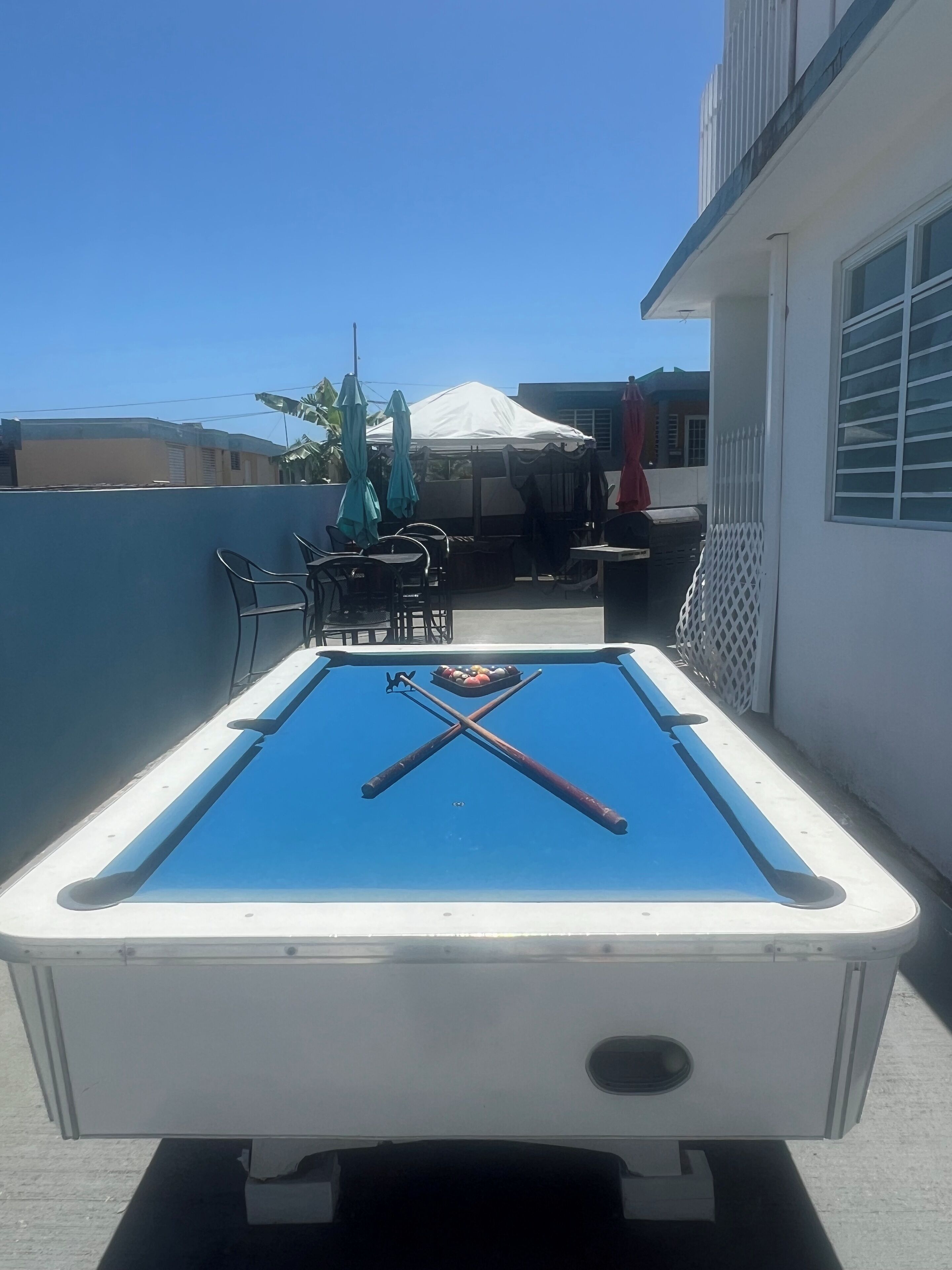 Une table de billard avec des queues et des billes, entourée de mobilier d’extérieur et d’une tente blanche.