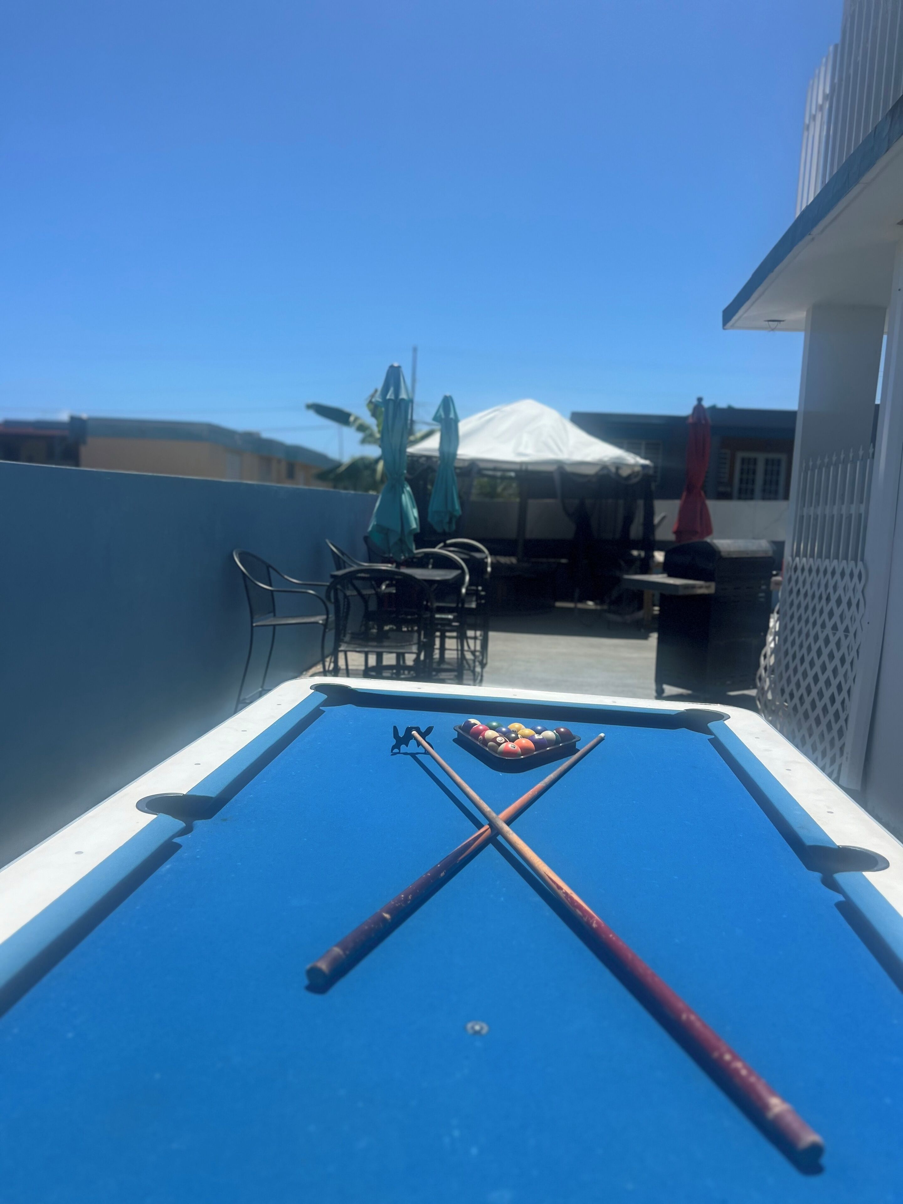 A pool table with pool cues and balls, outdoor seating, and a tent in the background.