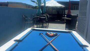 A pool table with pool cues and balls, outdoor seating, and a tent in the background.