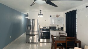 A compact kitchen with a stainless steel refrigerator, oven, and microwave. There is a dining area with a wooden table and chairs. - Jobos Luxury Condos (Isabela)