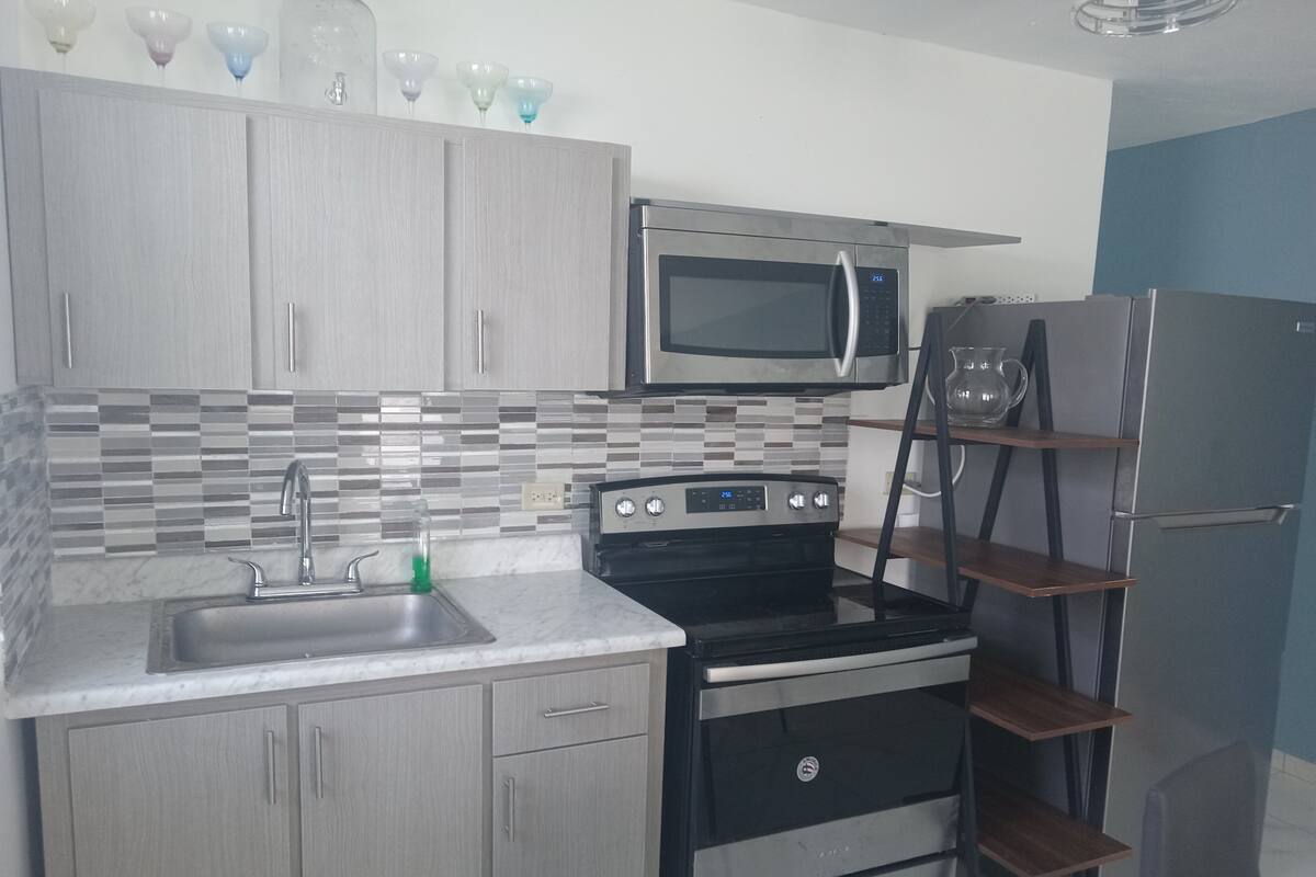 A kitchen with a microwave, oven, and refrigerator. There is a sink with a faucet, and a tiled backsplash.