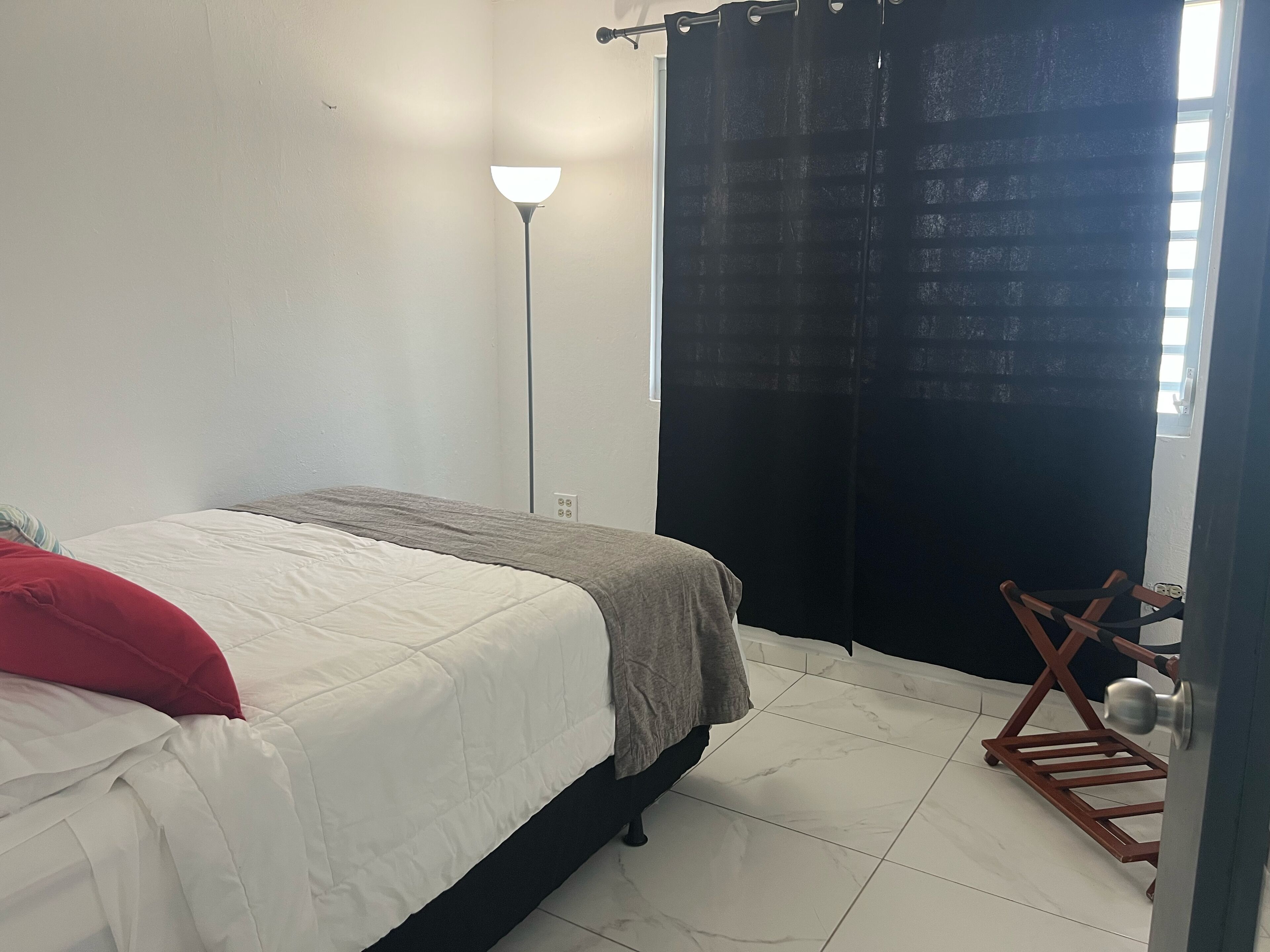 A bedroom with a bed, a floor lamp, a black curtain, and a wooden chair.