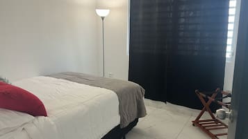 Un dormitorio con cama, lámpara de pie, cortina negra y silla de madera.