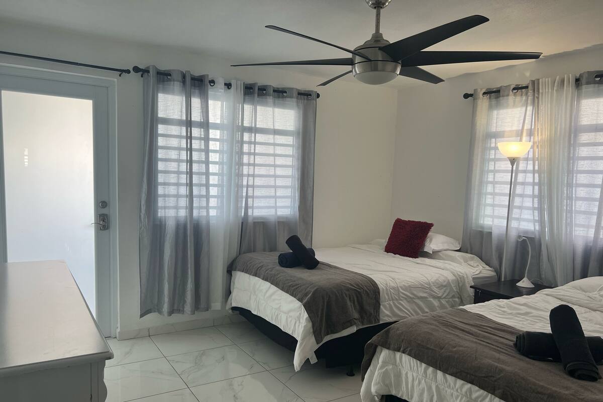 A hotel room with two beds, a ceiling fan, a desk, and a lamp.