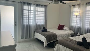 A hotel room with two beds, a ceiling fan, a desk, and a lamp.