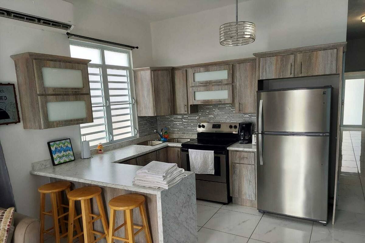 A modern kitchen with a stainless steel refrigerator, a built-in oven, and a large island with stools.