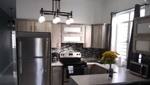 A modern kitchen with stainless steel appliances, wooden cabinets, a central island, and a hanging light fixture. - Jobos Luxury Condos (Isabela)