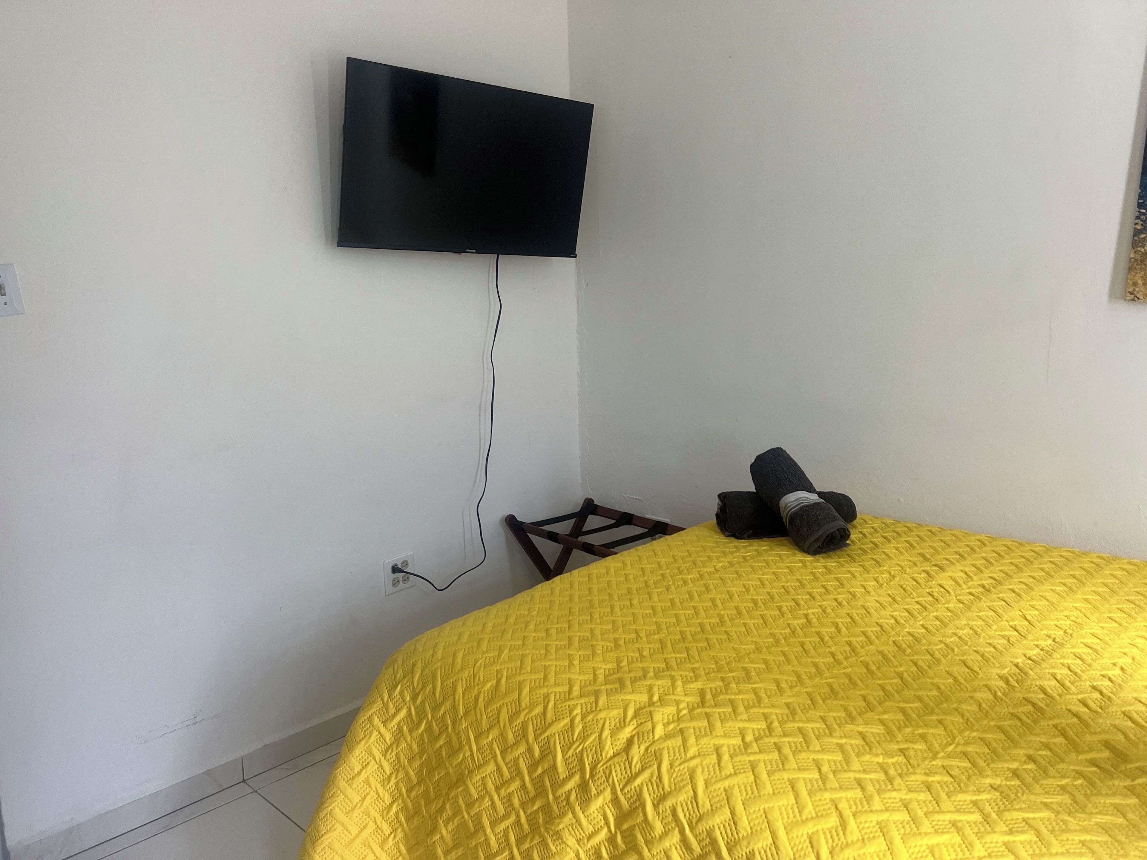 A room with a bed, a television mounted on the wall, and a power outlet.