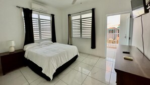 A bedroom with a bed, a ceiling fan, a TV, and a window with blinds. - Jobos Luxury Condos (Isabela)