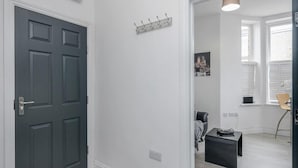 Un couloir avec une porte de couleur gris foncé, un porte-manteau et une petite table sur laquelle se trouve un ordinateur portable.