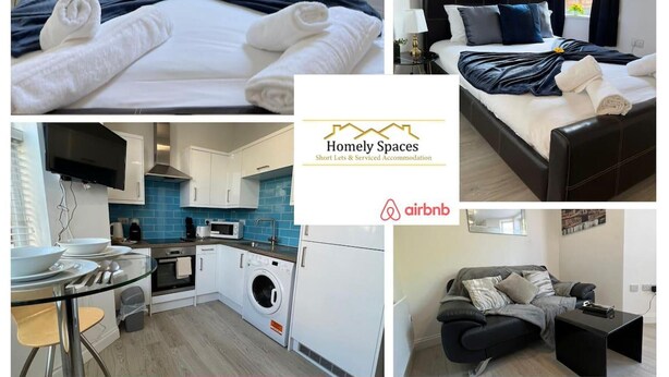 Une chambre d’hôtel comprenant un lit, une petite table avec une chaise, un coin cuisine avec un lave-linge, et un espace de vie avec un canapé et une table basse.