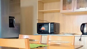 A compact kitchen with a wooden table, chairs, a microwave, a kettle, and a refrigerator.