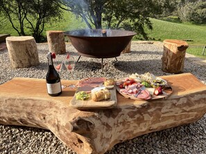 An outdoor barbecue setup with a grill, food, and drinks on a wooden table. - Meadows Farmhouse - Adelaide Hills (Meadows)