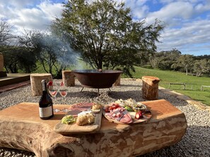 An outdoor barbecue setup with a grill, food, and drinks on a wooden table. - Meadows Farmhouse - Adelaide Hills (Meadows)