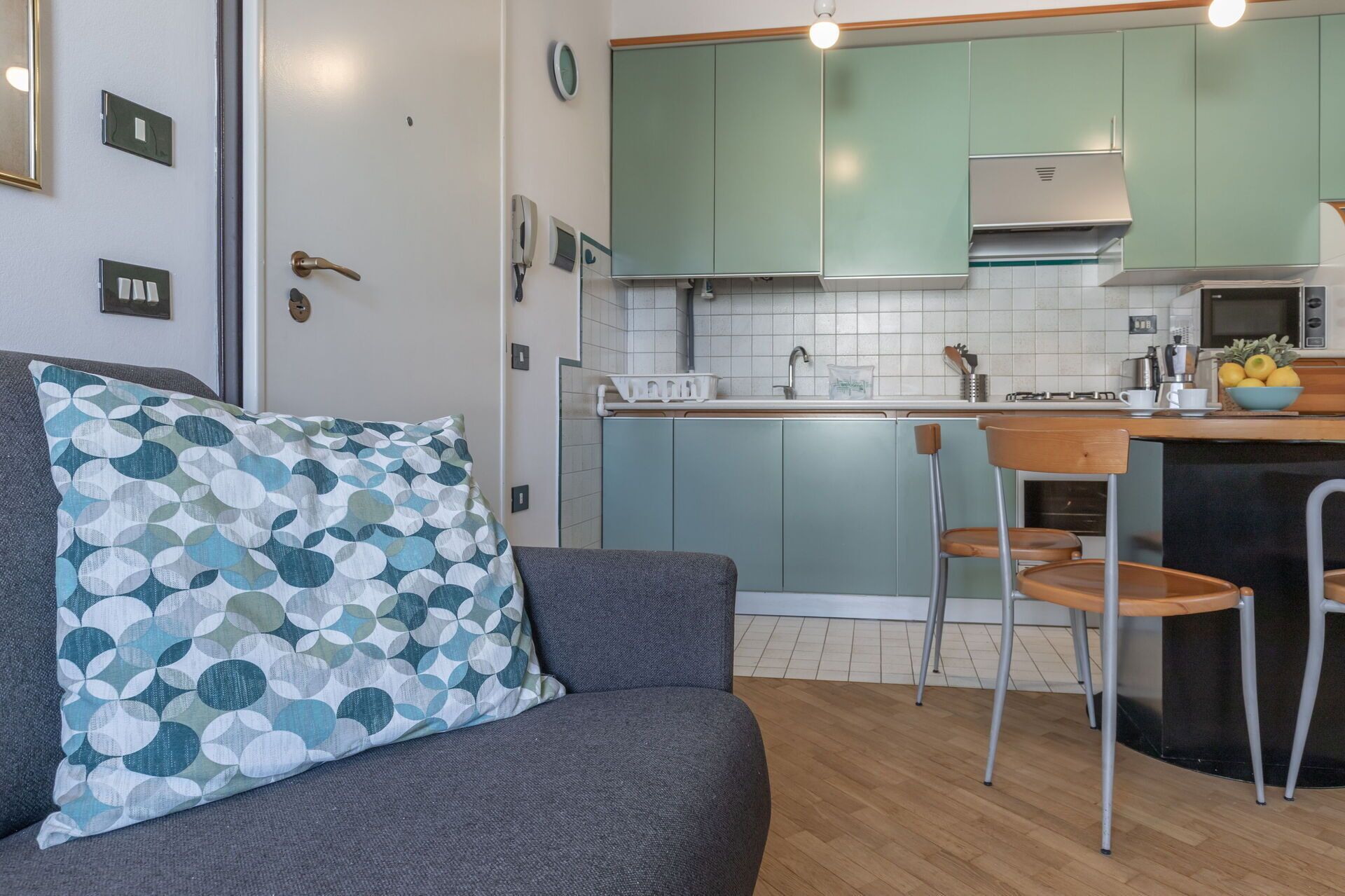 A compact living space with a kitchenette, a sofa with patterned cushions, and a dining area with chairs.