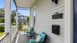 A porch with two chairs and a small table, a mailbox, and a house number sign.