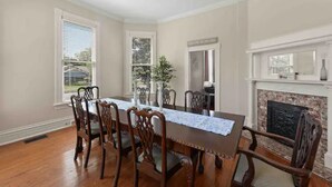 A dining room with a wooden table and chairs, a fireplace, and a window with blinds.