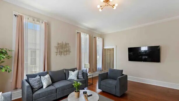 A modern living room with a grey sofa, a smaller grey armchair, a coffee table, and a flat-screen TV mounted on the wall.
