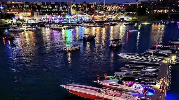 Uma marina à noite com barcos atracados e iluminados por luzes coloridas.