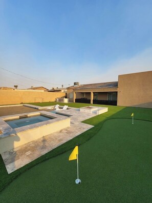 A residential property with a swimming pool, artificial green lawn, and a golf flag.