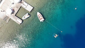 Eine Luftaufnahme einer Küstenlandschaft mit einem Pier, einem daran festgebundenen Boot und klarem türkisblauem Wasser.