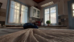 Ein Schlafzimmer mit Bett, einem Fenster mit Vorhängen, einer kleinen Topfpflanze und einer Küchenzeile mit Schränken und einem Herd.