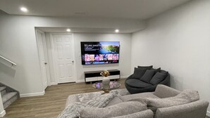 Een moderne woonkamer met een hoekbank, een flatscreen televisie aan de muur en een trap die naar een hoger niveau leidt.