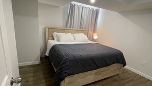 Een slaapkamer met een houten bed, witte gordijnen en een bedlampje.