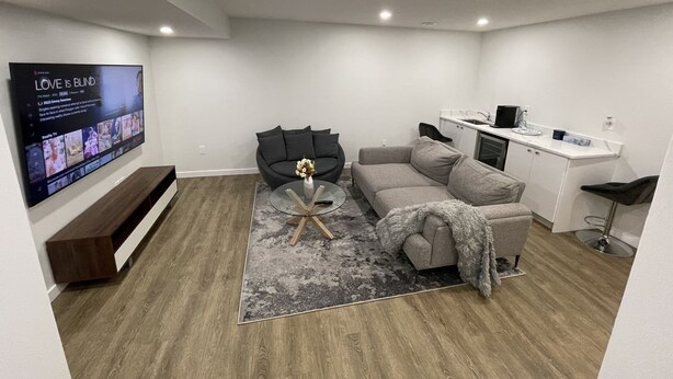 Een moderne woonkamer met een grijze bank, een salontafel en een flatscreen televisie aan de muur.
