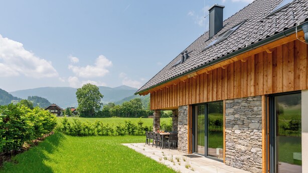 Een modern huis met een stenen gevel, houten buitenkant en een terras met zitplaatsen.