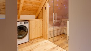 Een kleine, houten kamer met een wasmachine, een sauna en een glazen deur naar een sauna-ruimte.