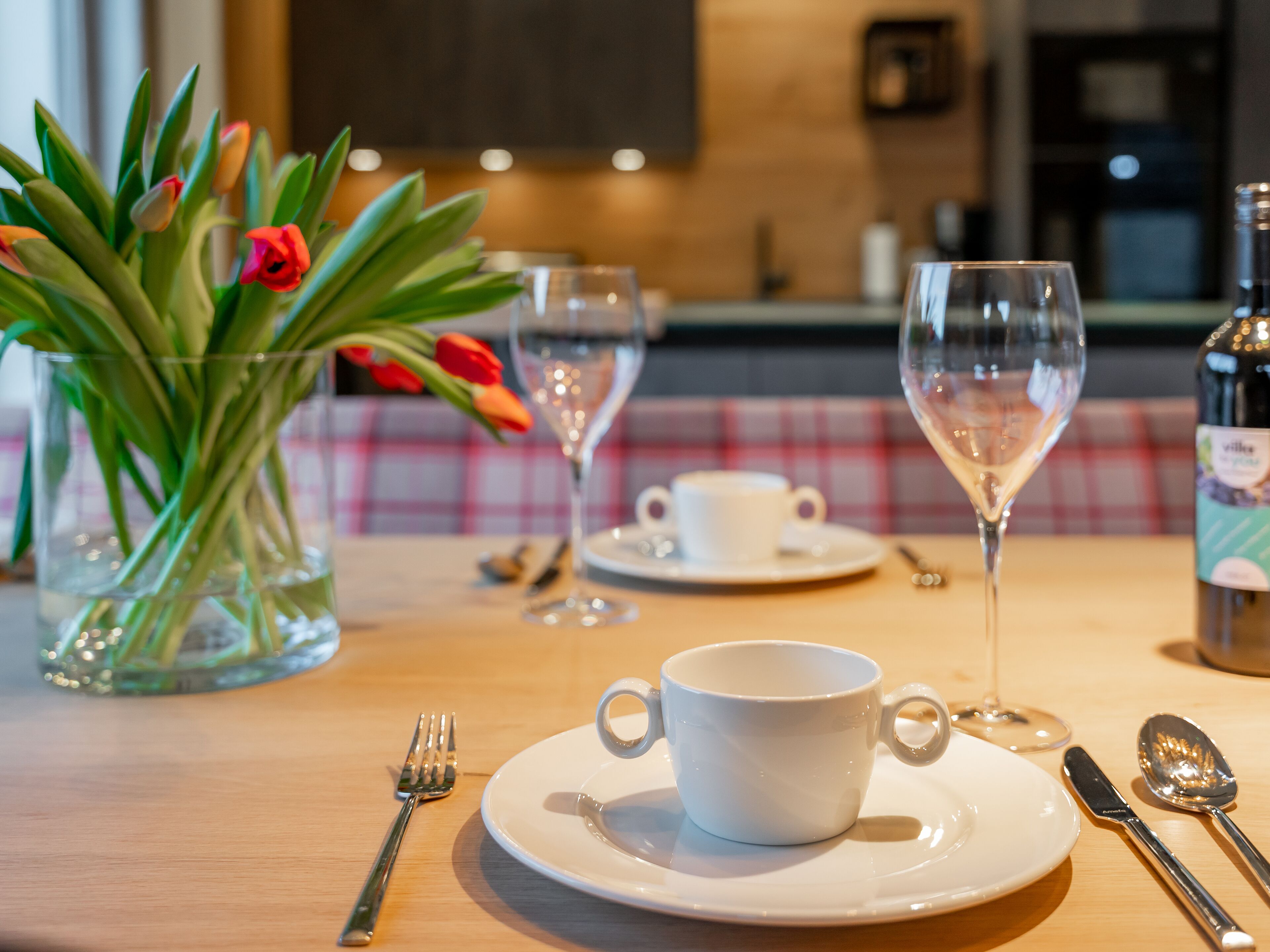 Una mesa de comedor con una taza blanca, un platillo y un vaso de agua. También hay un tenedor, un cuchillo y una cuchara sobre la mesa.