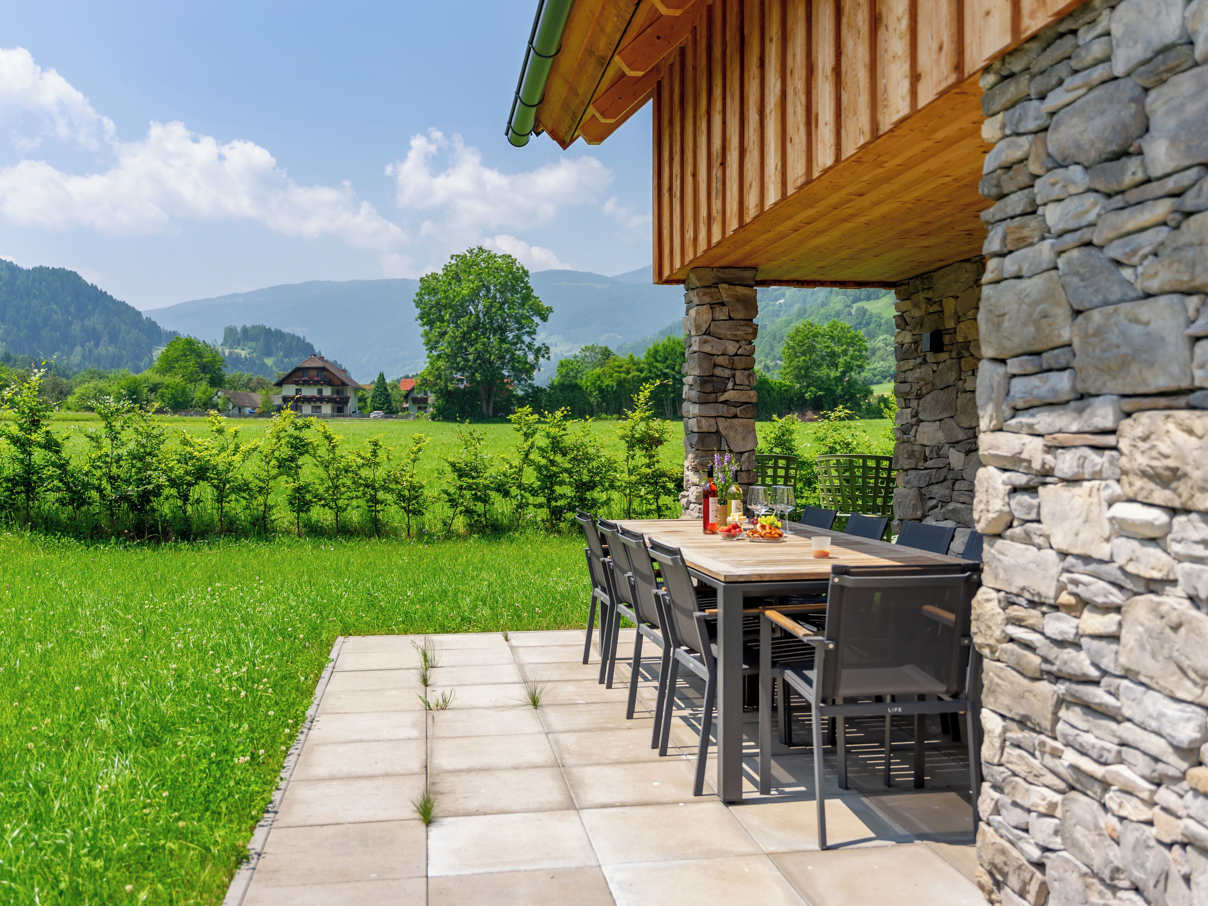 Un patio con una pared de piedra, una mesa de madera y sillas.