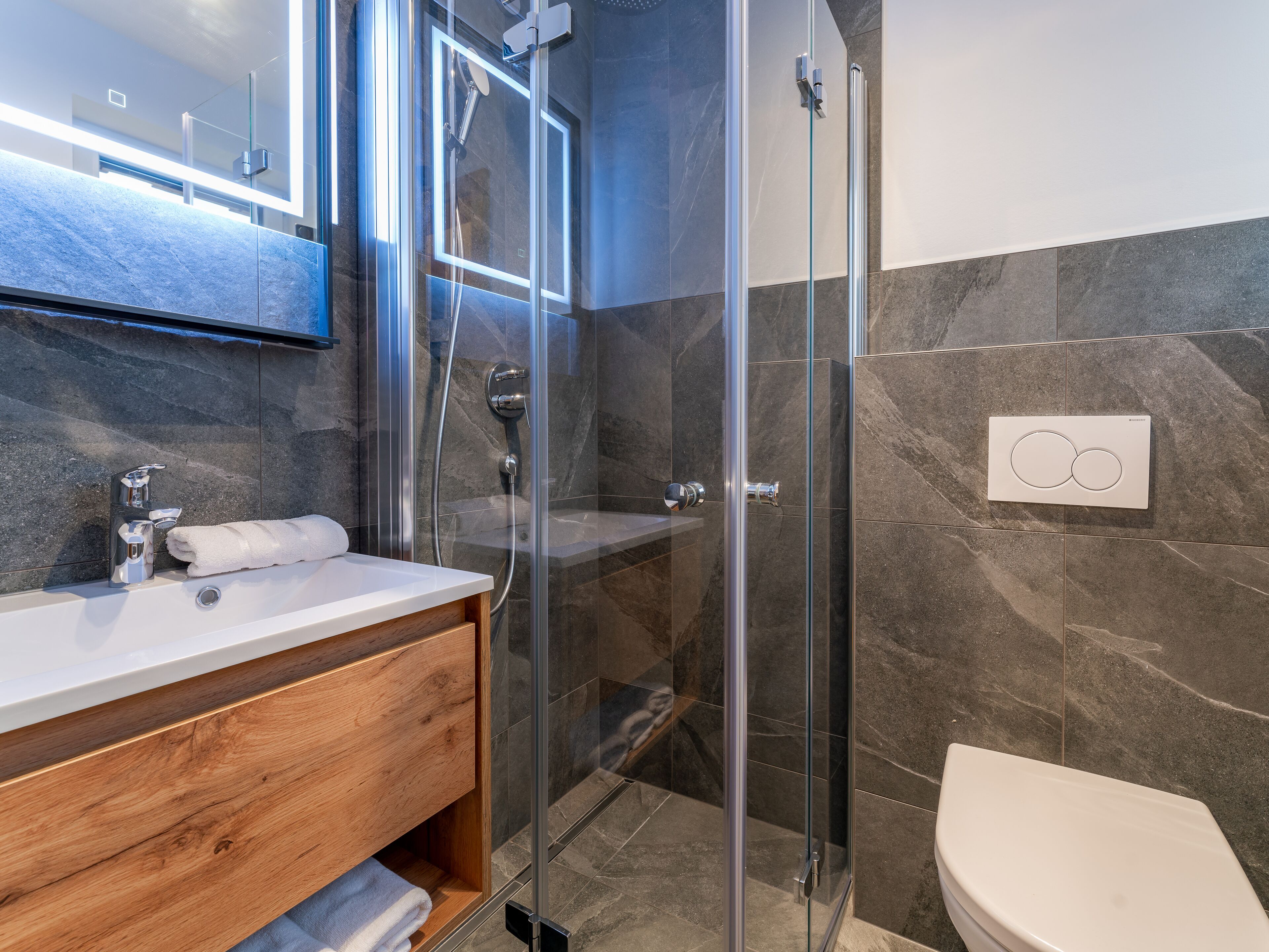 A modern bathroom with a glass-enclosed shower, a wooden vanity, and a white toilet.
