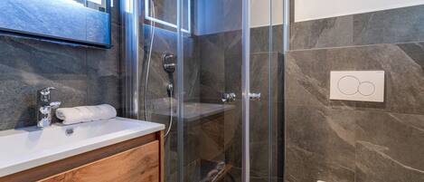 A modern bathroom with a glass-enclosed shower, a wooden vanity, and a white toilet.