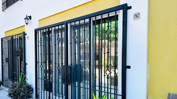 A building with a yellow and white facade, black metal gates, and a small potted plant. - Meson del capitan 8 depa en el centro! (Mazatlán)