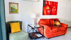 A living room with a green armchair, a red sofa, a glass coffee table, a white lamp, and a framed picture on the wall. - Meson del capitan 8 depa en el centro! (Mazatlán)