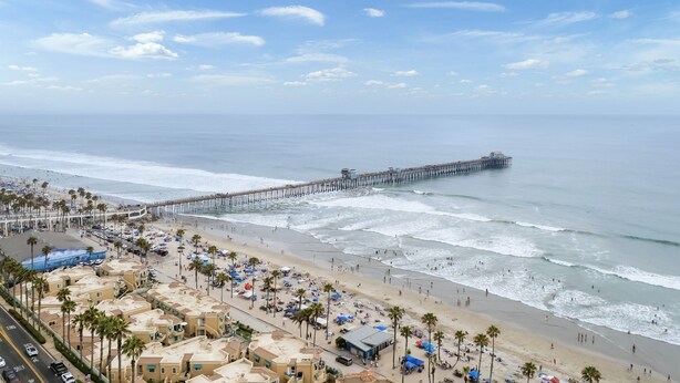 A beach with a long pier extending into the ocean, a sandy shore with palm trees, and beach umbrellas. - Pet-friendly! Near downtown Oceanside - Sea Spray (Oceanside)